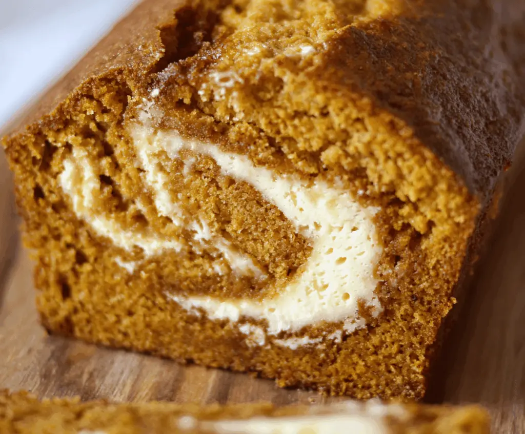 Delicious homemade pumpkin bread with creamy cream cheese swirl topped with nuts, perfect for fall baking.