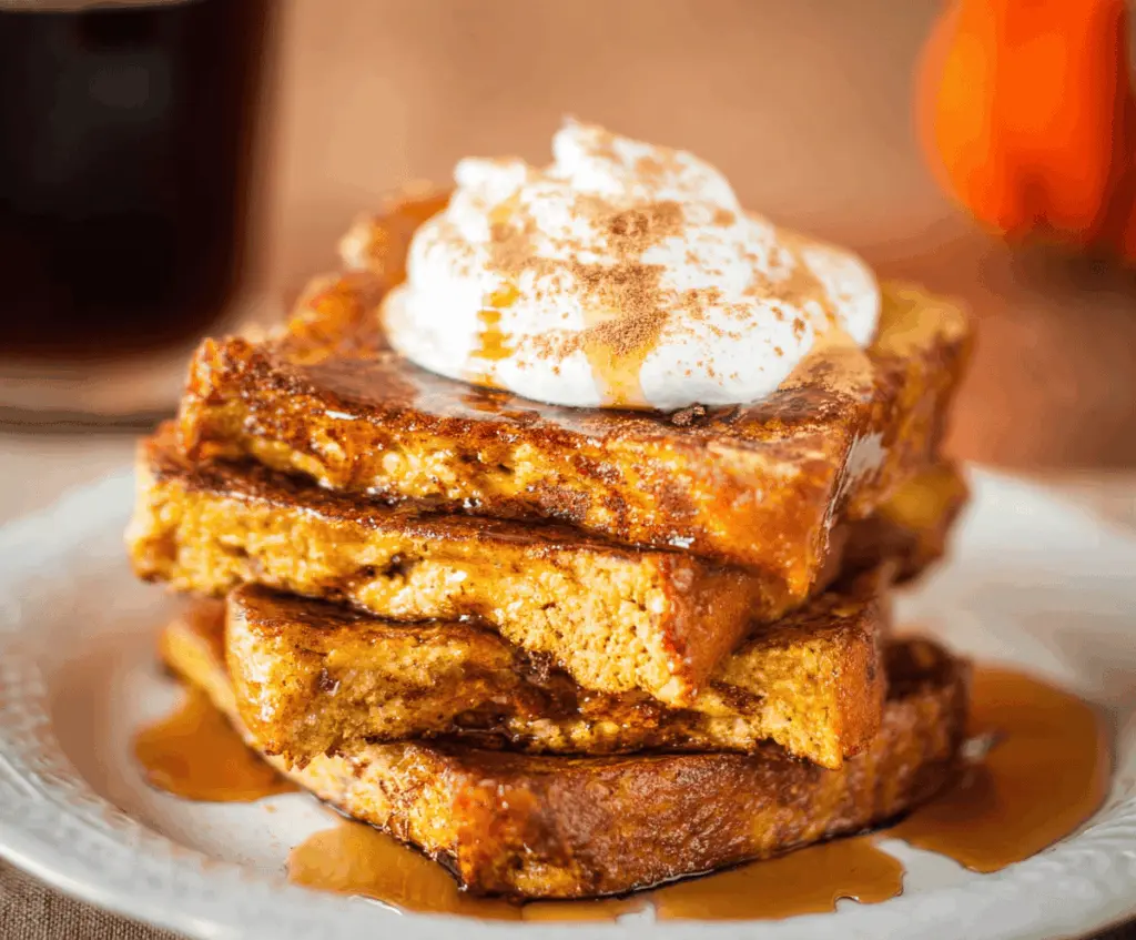 Golden Pumpkin Pie French Toast topped with whipped cream and cinnamon, served with maple syrup for a delicious breakfast treat.