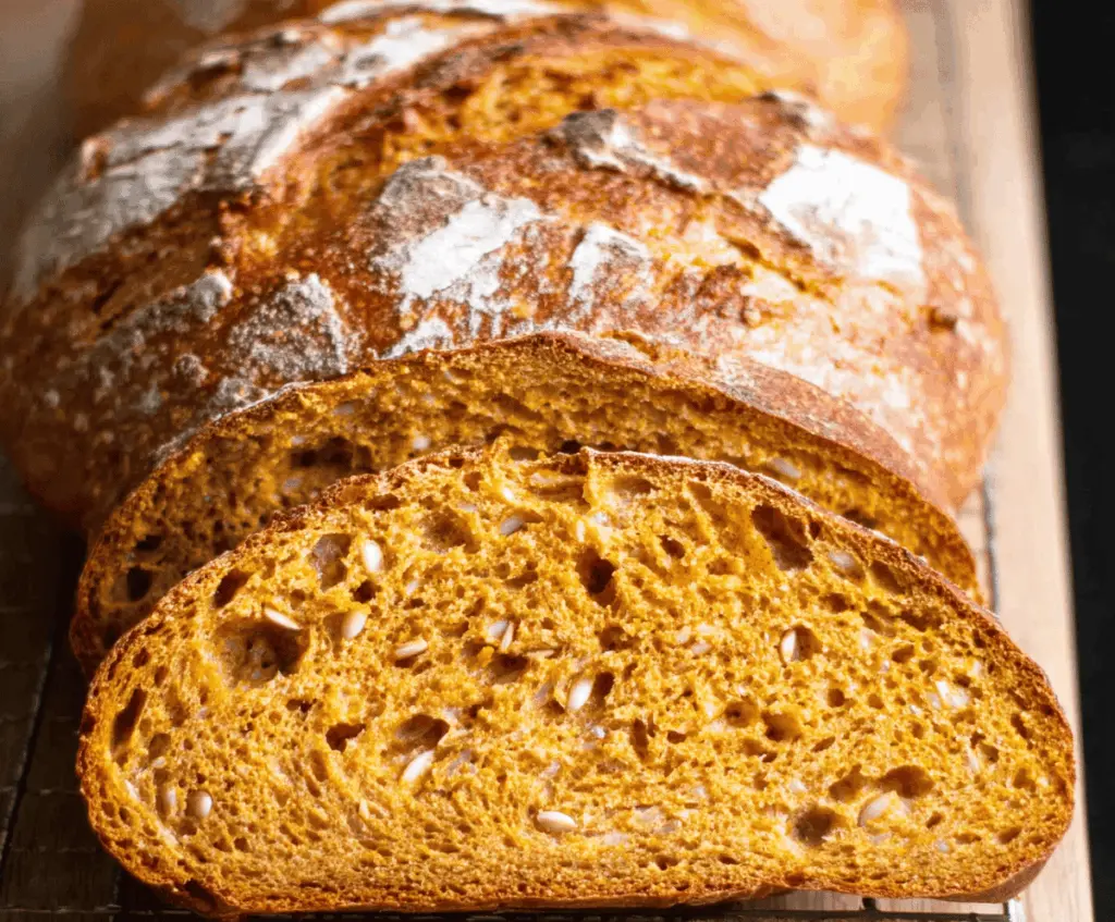 Golden pumpkin sourdough bread sliced open, revealing a moist, orange interior with a crunchy crust, perfect for fall baking.