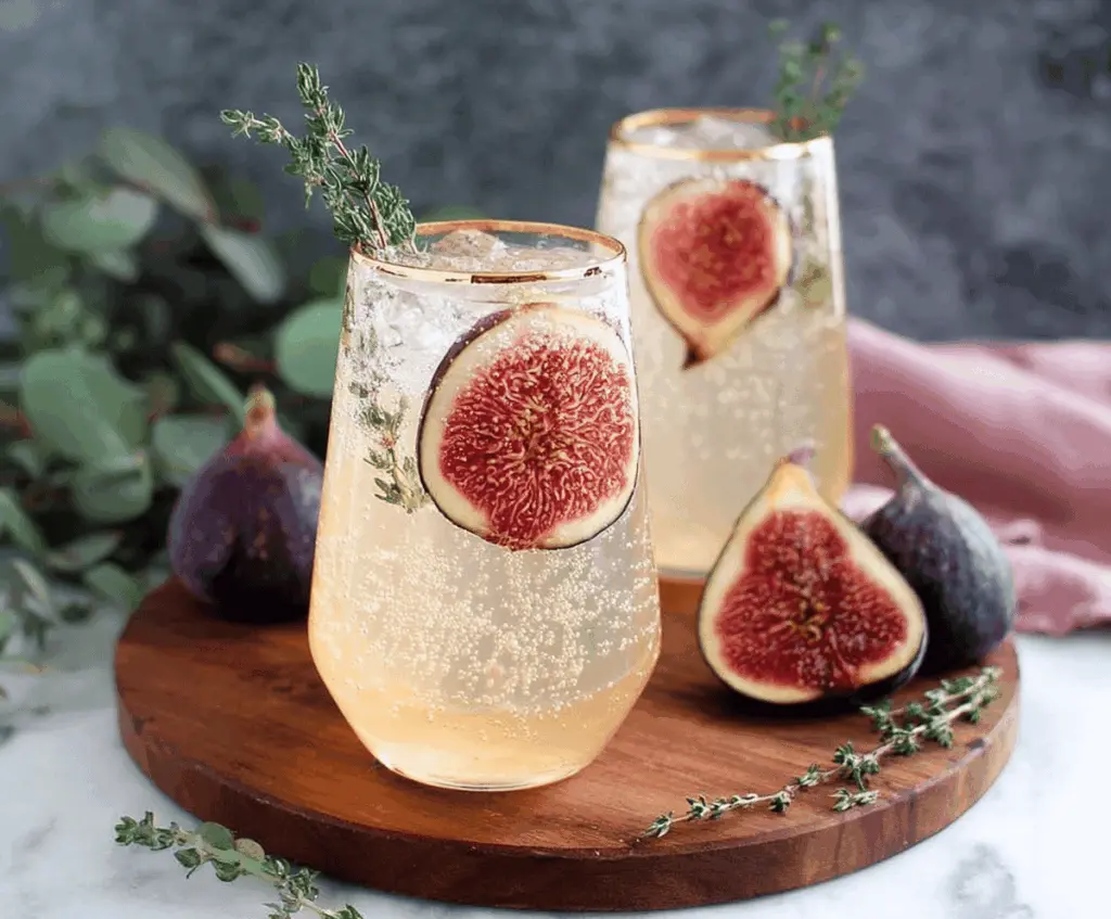 Refreshing Vanilla Fig Sparkler cocktail garnished with fresh figs and mint, served in a clear glass with ice, perfect for summer celebrations.