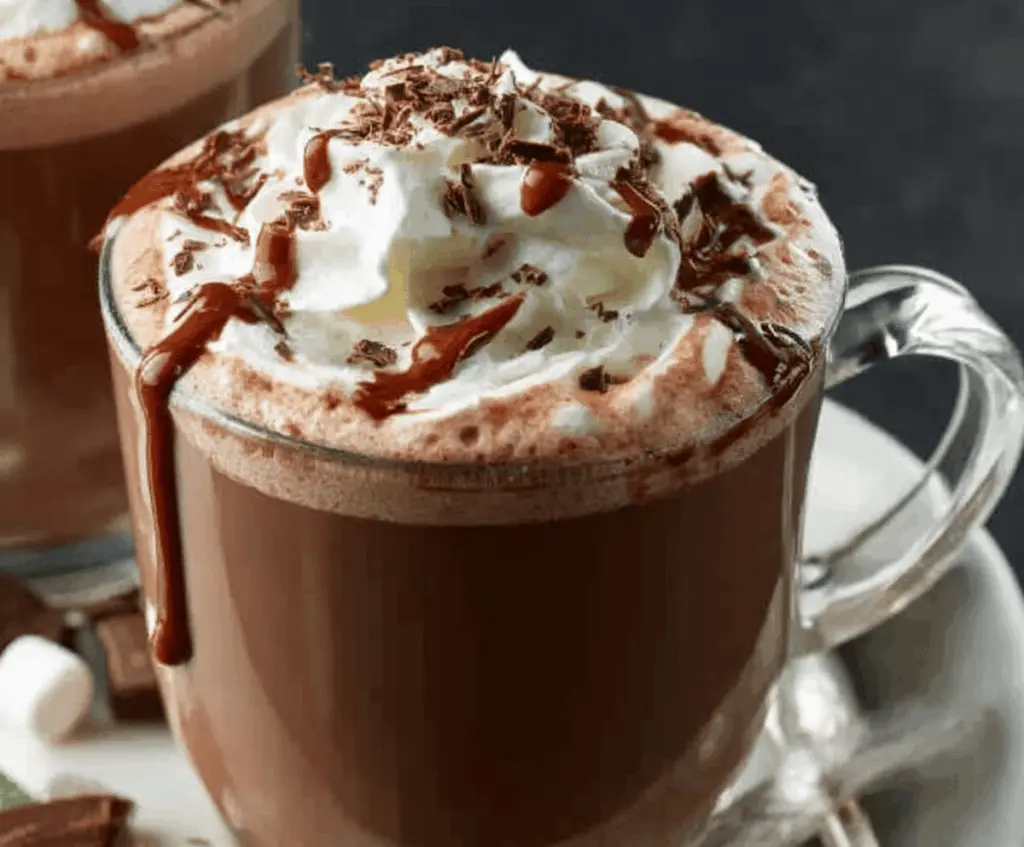 Creamy crockpot hot chocolate topped with whipped cream and marshmallows in a cozy setting
